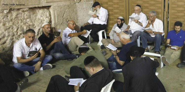 Group of men sitting on a floor while reading a book.