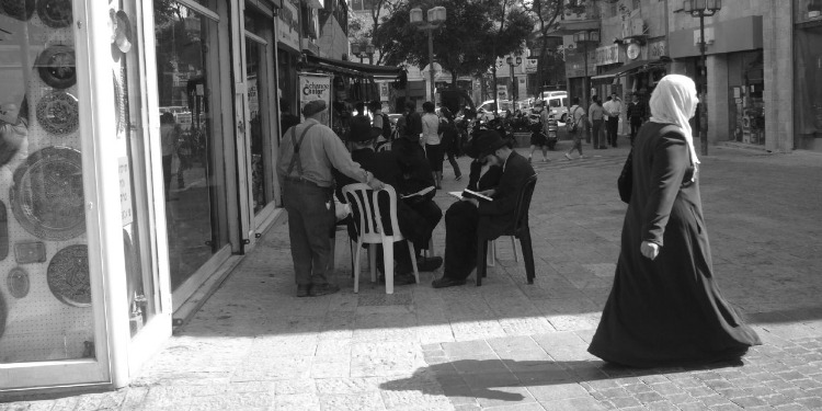 A woman crossing the street while others are sitting and reading or walking around a plaza.