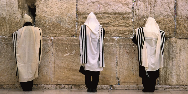 Three men in prayer shawls praying at the Western Wall.