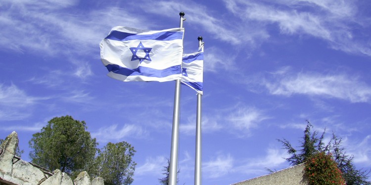 Two Israeli flags waving with a cloudy sky behind them.