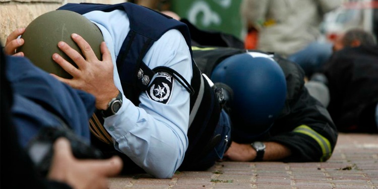 Two policemen with helmets on with their heads down and on the ground as they cover for safety.