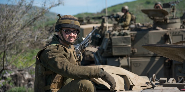 A young soldier in a full uniform and helmet while on top of a tank.