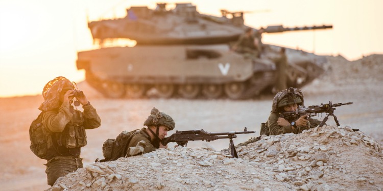 Three IDF soldiers on a stakeout with their weapons poised.