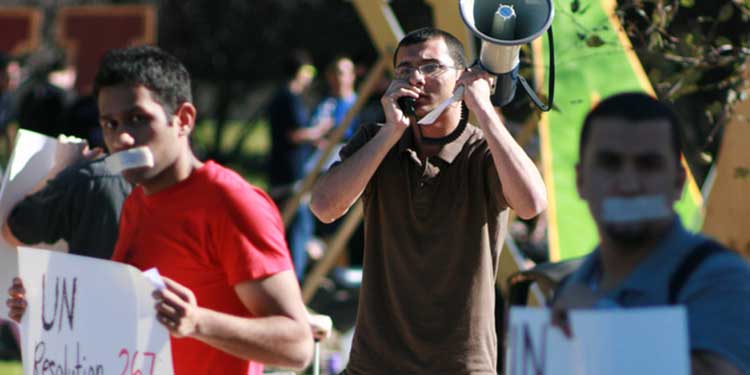 Group of young men during a protest holding a megaphone and white signs.