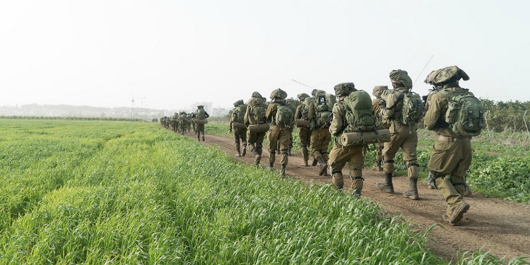 Line of soldiers walking through a dirt trail in the middle of a grass field.