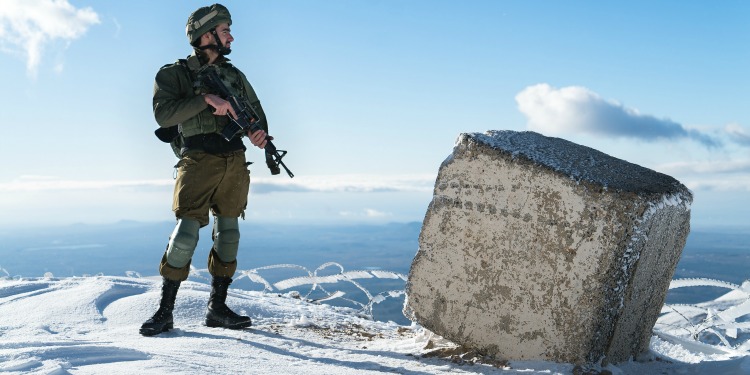 Soldier holding a gun on top of a snowy mountain.
