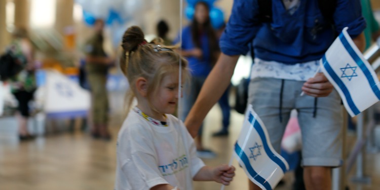 Young girl with hair in a bun wearing an oversized Fellowship shirt waving an Israeli flag.