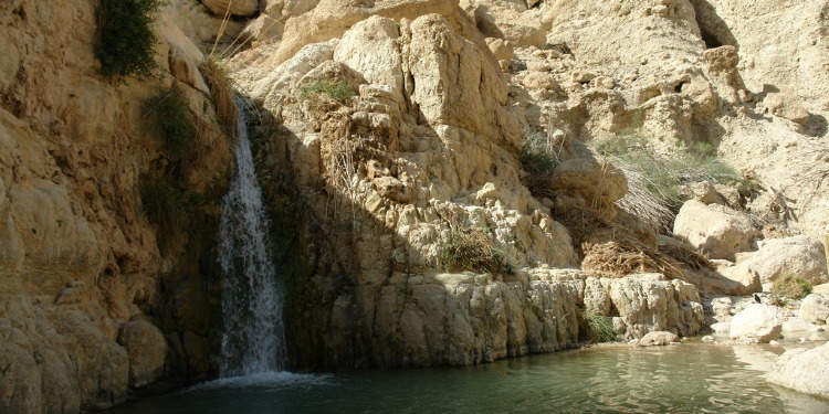 Small waterfall flowing into a small body of water with rocks behind and beside it.