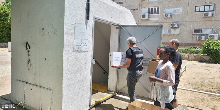 Two men holding IFCJ food boxes entering a building.