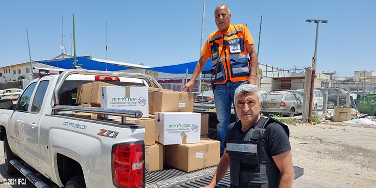 Two men standing on a truck that's loaded with IFCJ food boxes.