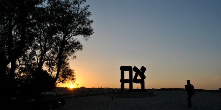 A sculpture and tree outlined by the sunset.