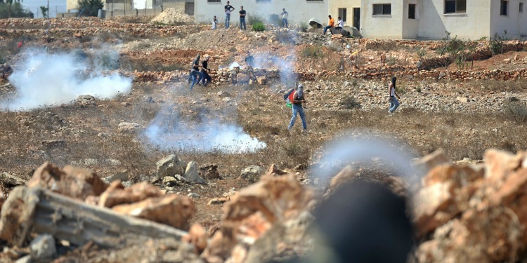 Young men walking in a field full of rocks, dirt, and smoke.