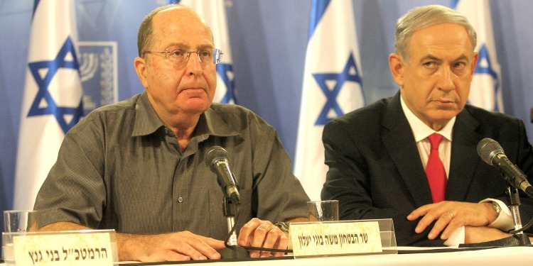 Bibi sitting alongside another man with microphones in front of them and Israeli flags behind them.