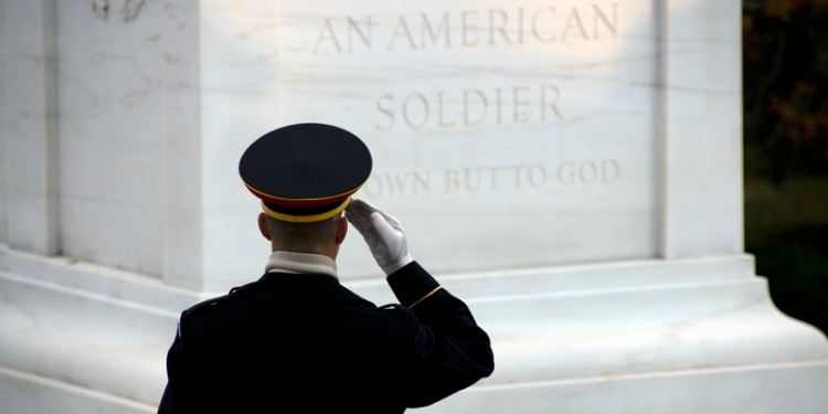 Soldier in his dress uniform saluting a memorial.