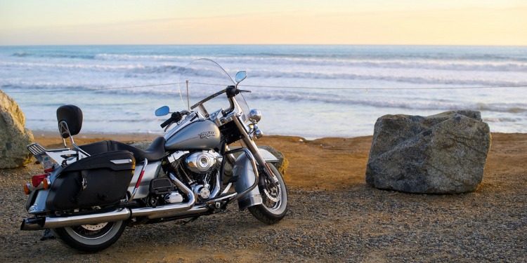 A motorcycle parked alongside the beach while the sun is about to set.