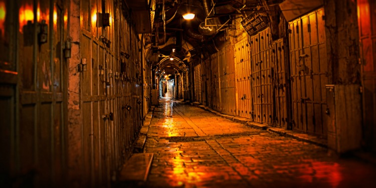 A dark walkway with locked doors and dim overhead hanging lights.