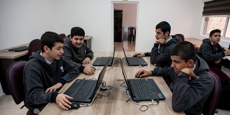 Four teens sitting together on laptops.