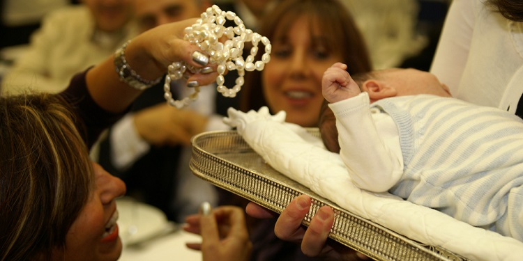 A woman holding pearls by a baby's head.