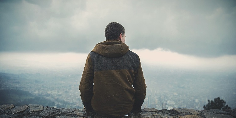 A man in a jacket sitting on a rock while overlooking a city.