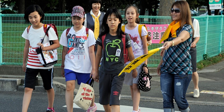 A mom helping a group of young girls cross the street.