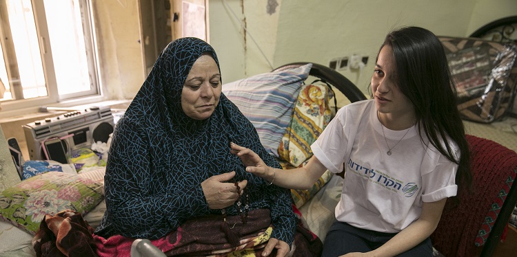 An IFCJ volunteer sitting with an elderly woman.