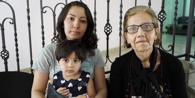 Two women sitting with a young girl on a bench.