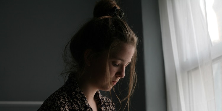 A sad young girl looking out a white window.