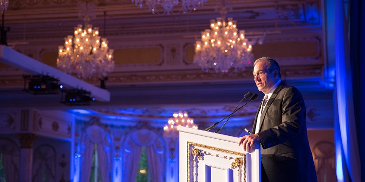 Rabbi Eckstein giving a speech at a white and gold podium.