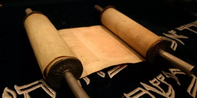 Open scroll with the torah on it on a gold and black patterned cloth.