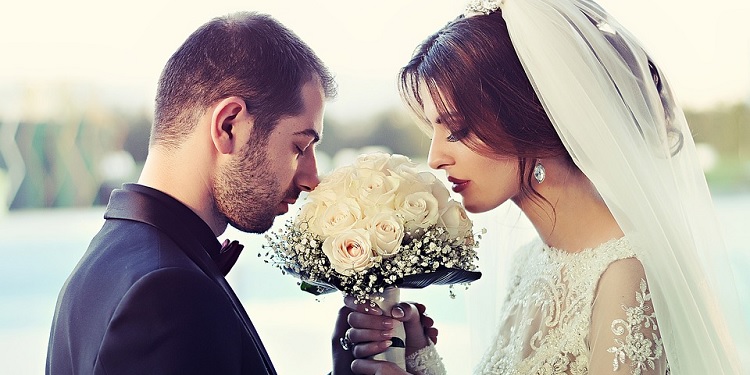 Wedding couple facing together while smelling a bouquet of flowers.