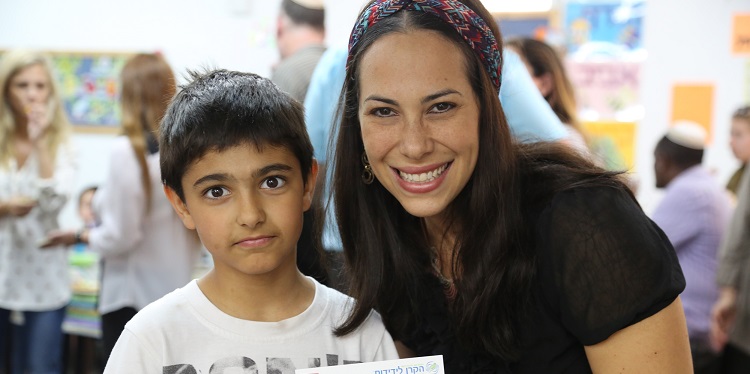 Yael Eckstein smiling next to a boy in a classroom.