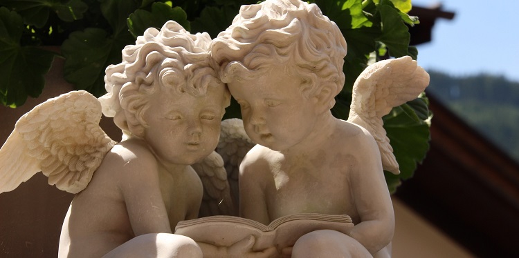 Statue of two young angels reading through a book.