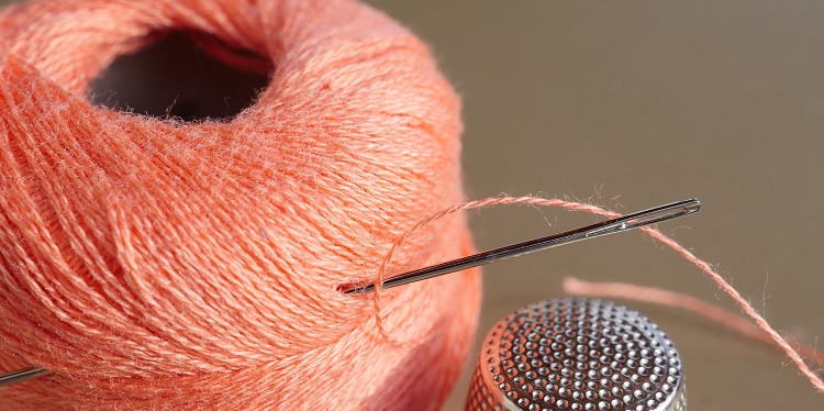 Close up of a needle in an orange spool of yarn.