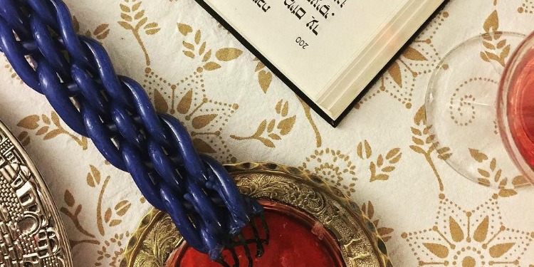 Close up image of a candle and book on a patterned tablecloth.