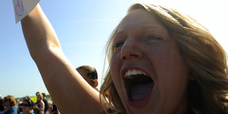 Woman holding a sign while screaming amongst a crowd.