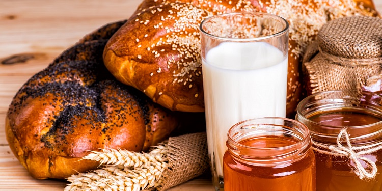 Bread, milk, honey, and wheat laid out on a table.