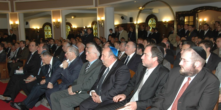 Several men wearing kippahs while sitting in a synagogue.