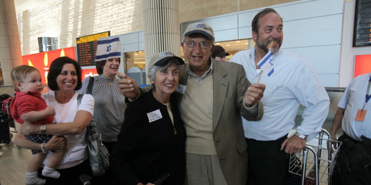 Elderly Jewish couple holding Israeli flags while standing in front of Rabbi Eckstein.