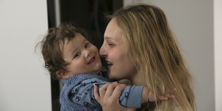 Young mother holding baby up to her face while smiling