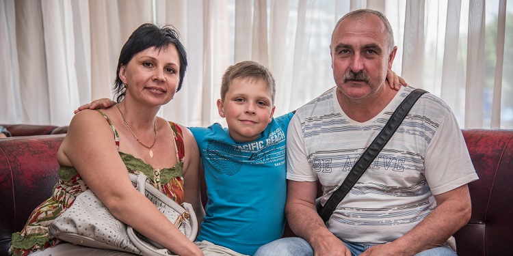 A family of three sitting on a red couch together.