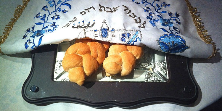 Challah on a serving platter covered with a white and blue cloth.