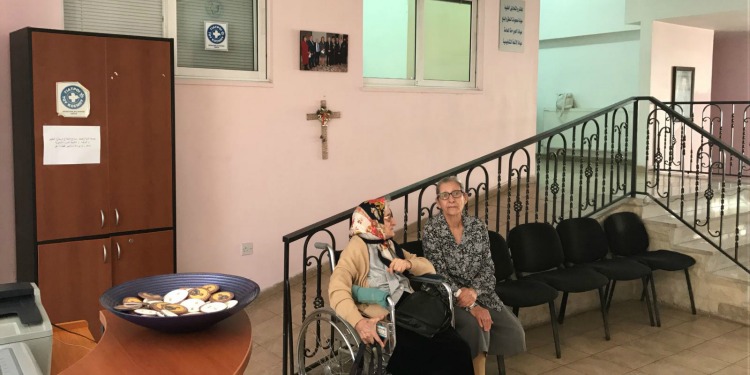 Two women sitting together, one in a wheelchair at a clinic.