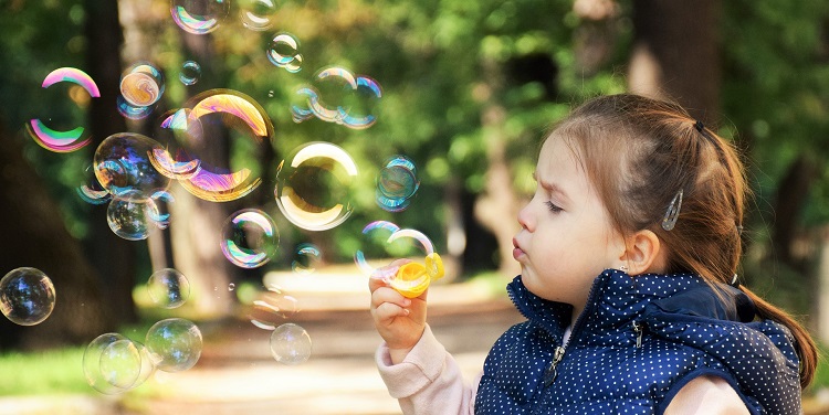 Young girl blowing bubbles while standing outside on a walking trail.