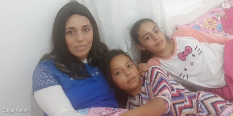 A mother and her two daughters all leaned up against a wall together.