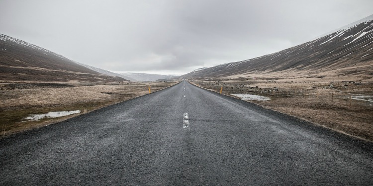 A two-way street in between two mountains covered with dirt and snow.