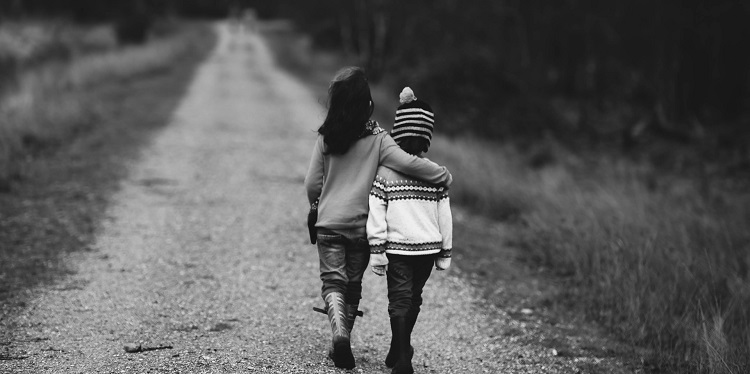 Two young children walking along a dirt trail outside.