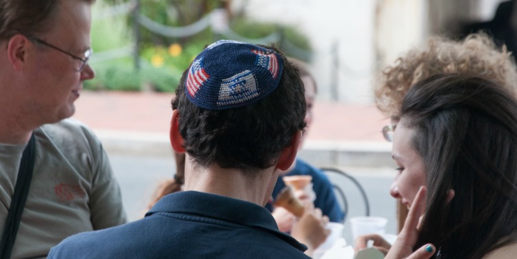 The back of a family eating ice cream together, while focus is on the son of the family in an American and Israeli flag patterned kippah.