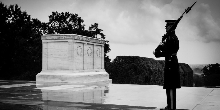 A soldier holding a bayonet outside of a memorial on a cloudy day.