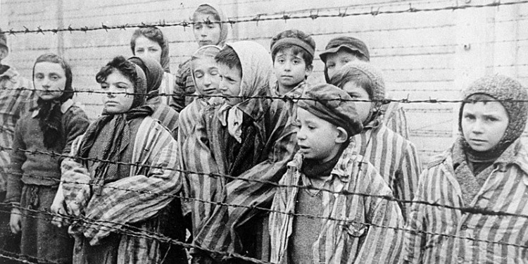 Black & white photo of young children behind a barbed-wire fence in Auschwitz
