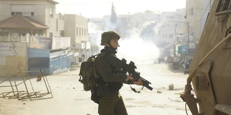 A soldier holding a weapon as he patrols the street.